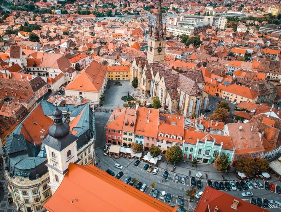 Aerial view of Sibiu's old town — orange rooftops, the Lutheran cathedral spire, and the Small Square